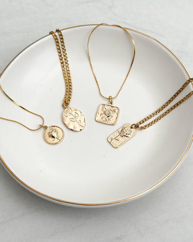 All 4 gold flower necklaces sitting on a cream colored plate